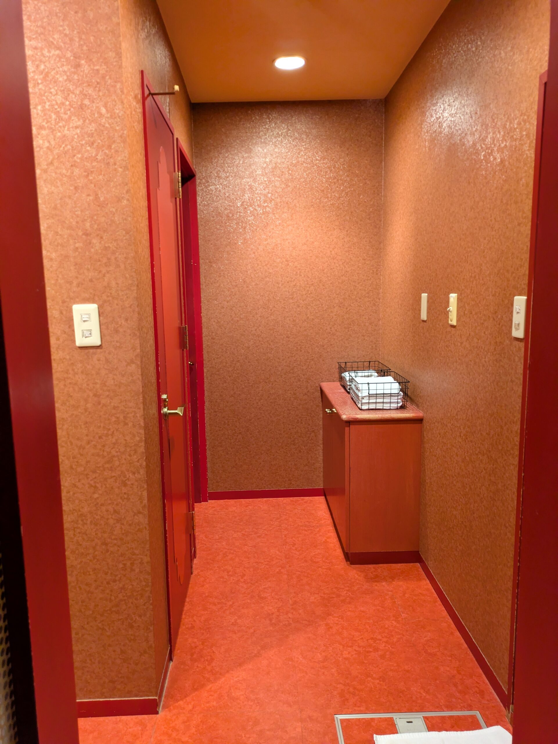 Hotel ARUN 客房內走道:紅粉色系牆面、獨立房門與備有乾淨毛巾的邊櫃