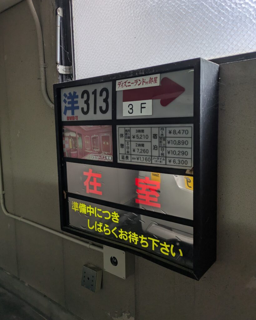 ホテルロンシャン313号室の駐車場にある案内パネル。「洋313」「ディズニーランドの部屋」「3F」と表記され、利用料金表や赤い文字で「在室」と表示されている。
